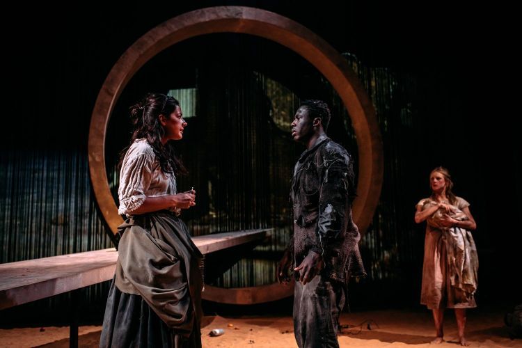 Actors on the set of The Wheel, with a large circular piece of concrete and long platform and video projected backdrops
